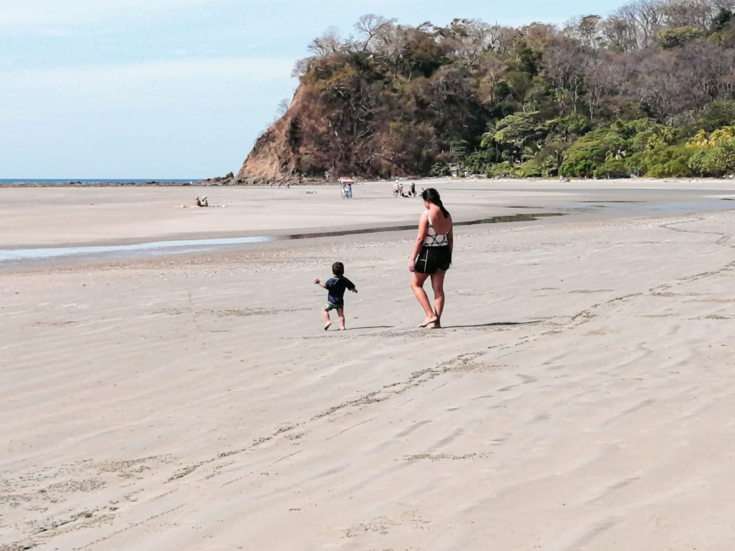 A sandy beach with a woman and a child walking.