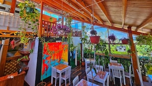 Un patio interior con vigas de madera, sillas blancas y plantas colgantes.