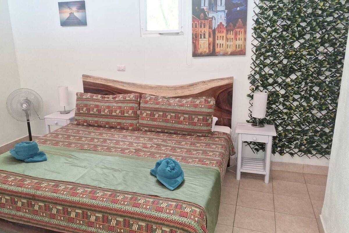 Una habitación con dos camas, un ventilador, una mesita con lámpara y una pared con un estampado de hojas.