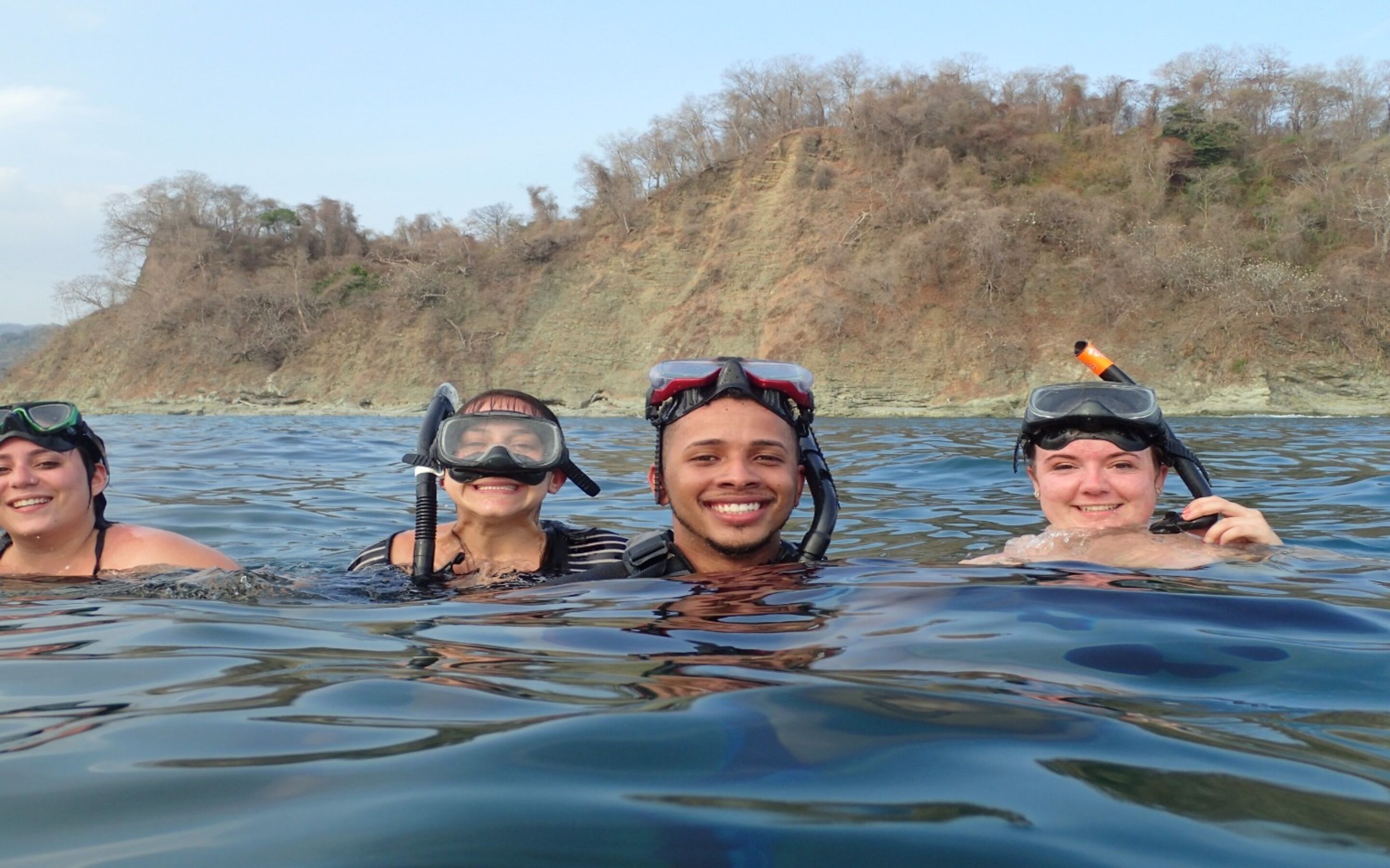 Three people snorkeling in a body of water with a hilly landscape in the background.
