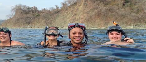 Three people snorkeling in a body of water with a hilly landscape in the background.