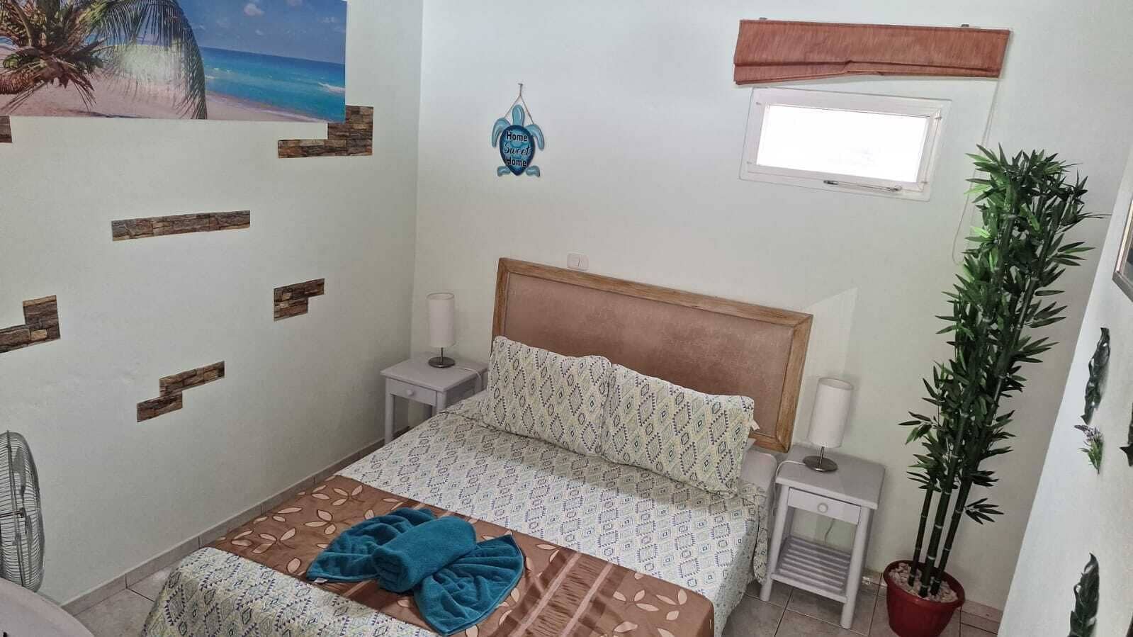 A bedroom with a bed, bedside tables, a window, a wall decoration, and a potted plant.
