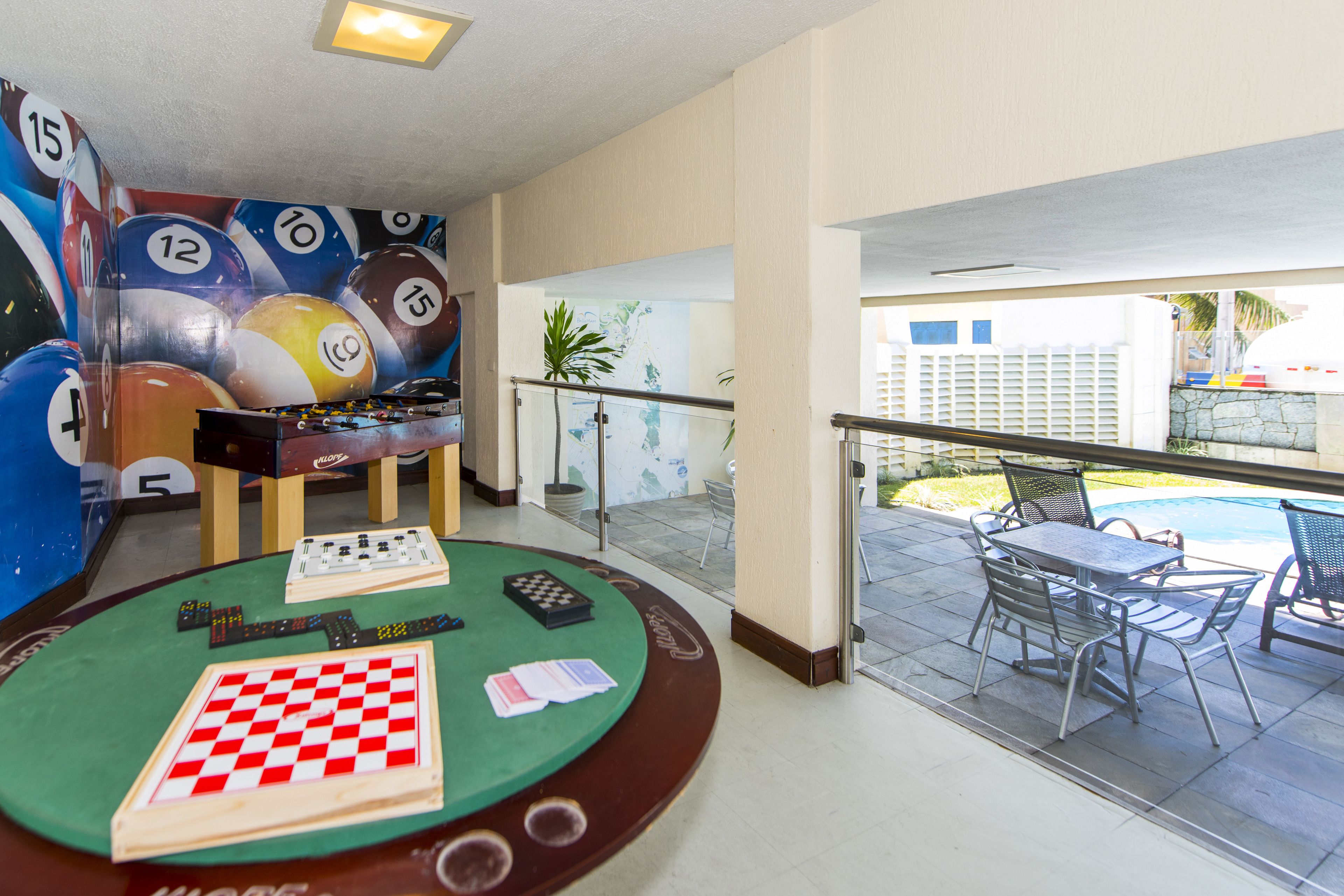 A pool table with various games, a pool table in a room with a mural of pool balls, and a balcony with outdoor seating.