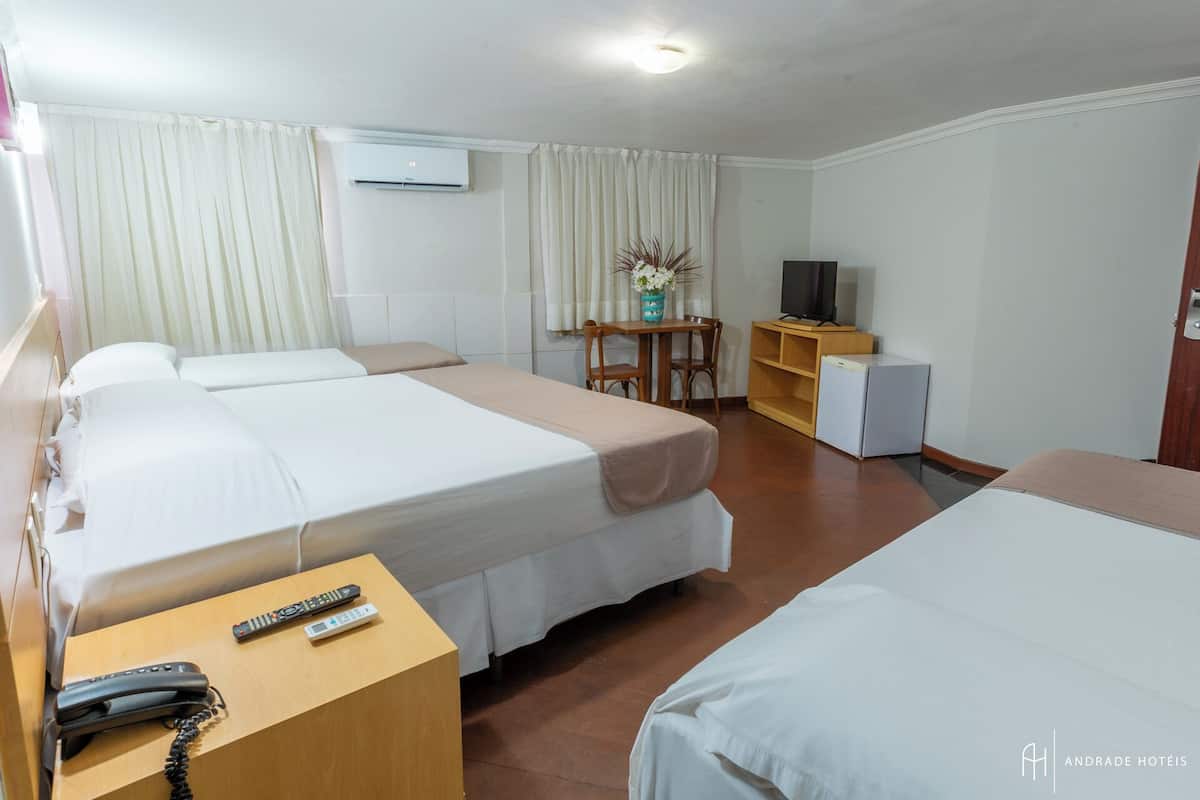Quarto de hotel com duas camas, uma escrivaninha com telefone, uma mesinha com um vaso, televisão e frigorífico.