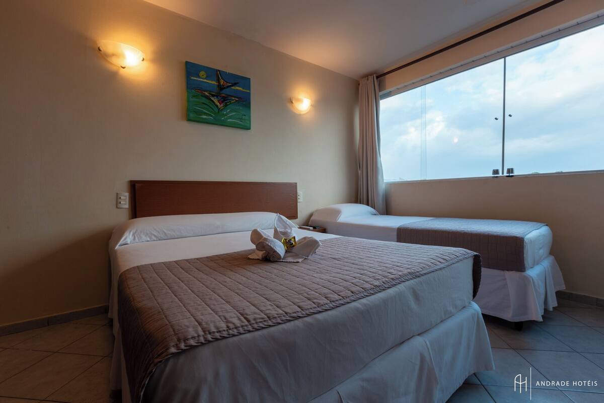Quarto de hotel com duas camas, uma janela grande e um quadro na parede.