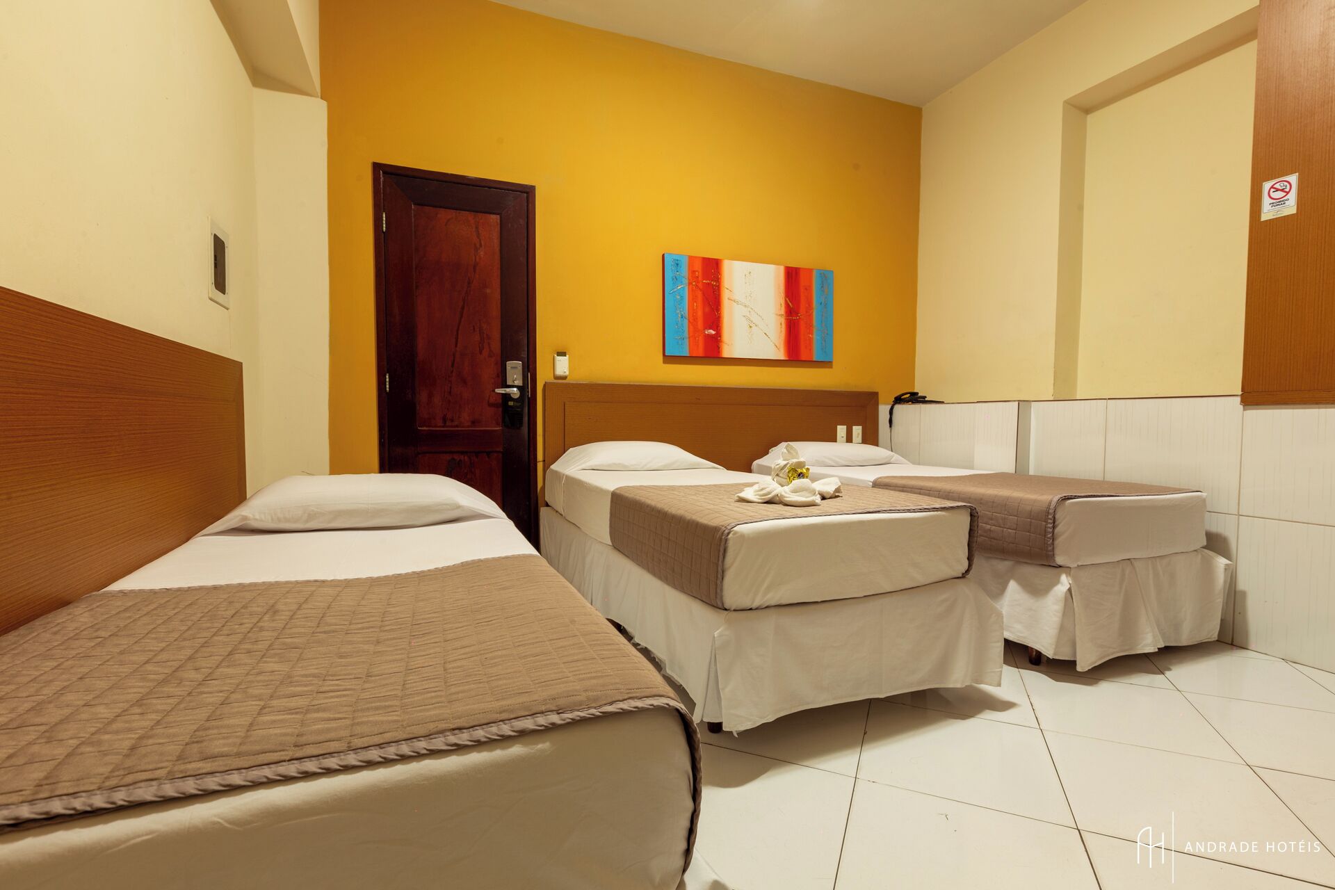 A hotel room with two single beds, a wooden headboard, a door, and a colorful abstract painting on the wall.