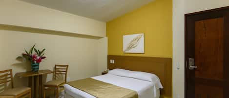 Una camera d'albergo con un letto, una scrivania, due sedie, un tavolino con un vaso di fiori e una porta.