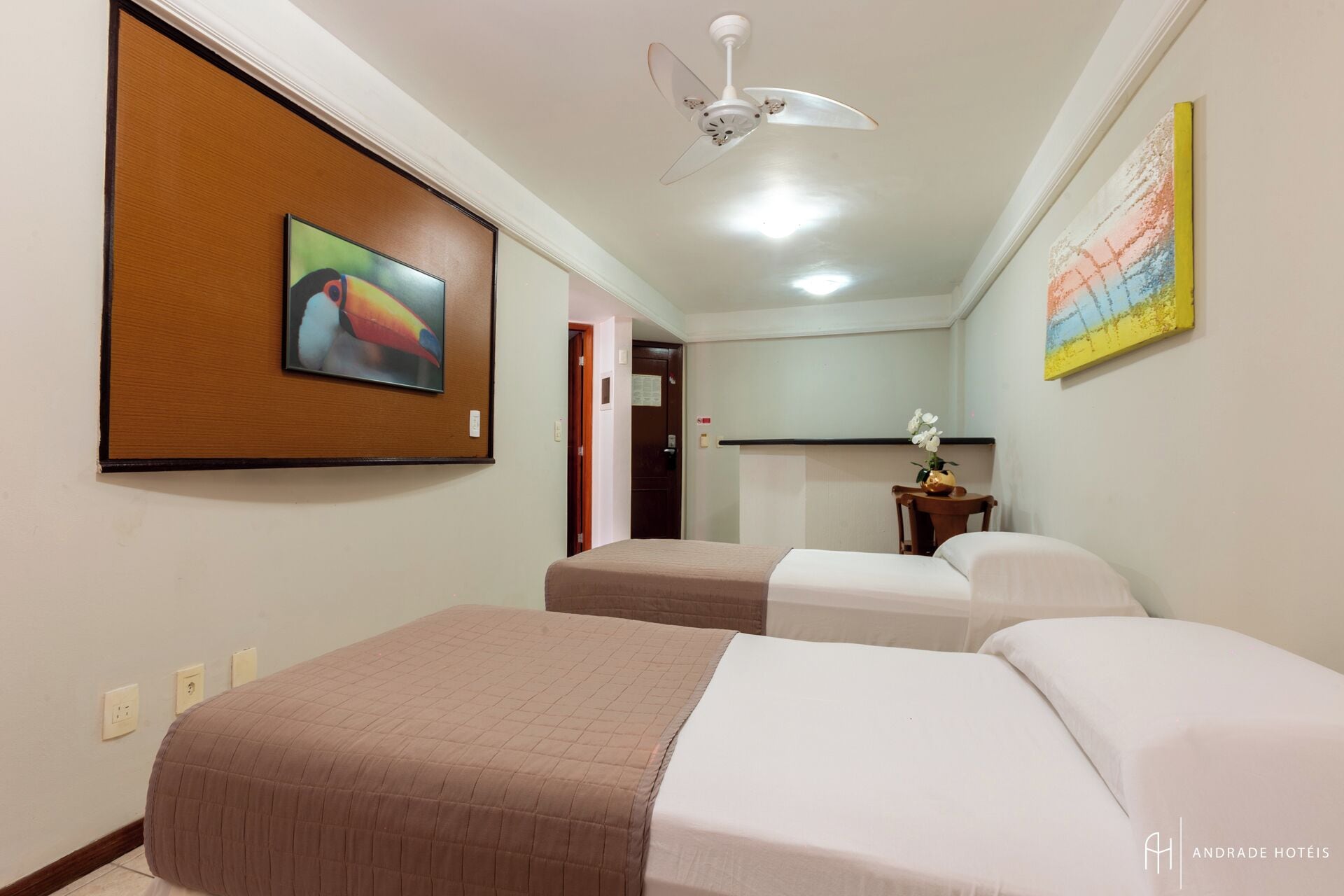 Una habitación de hotel con dos camas, un ventilador de techo, un cuadro en la pared y un florero con flores.