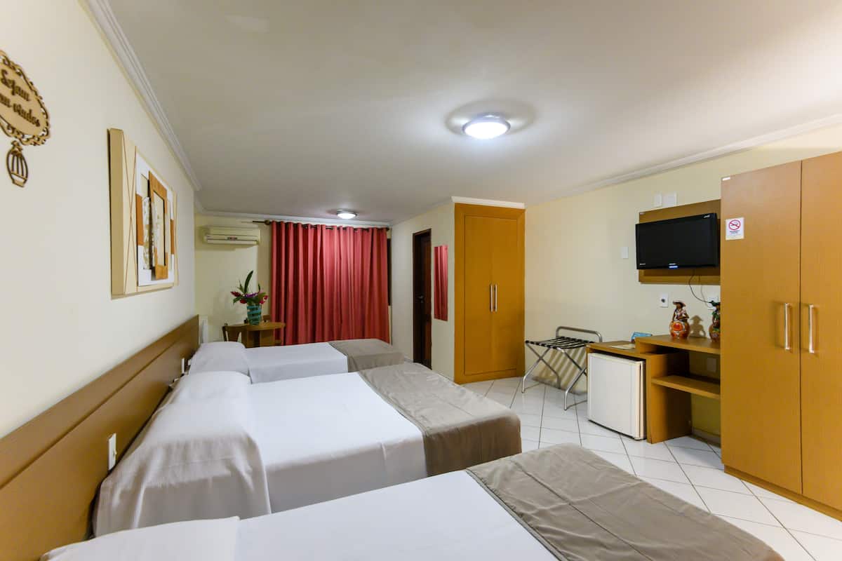 Quarto de hotel com três camas de solteiro, uma kitchenette pequena, televisão e guarda-roupa.