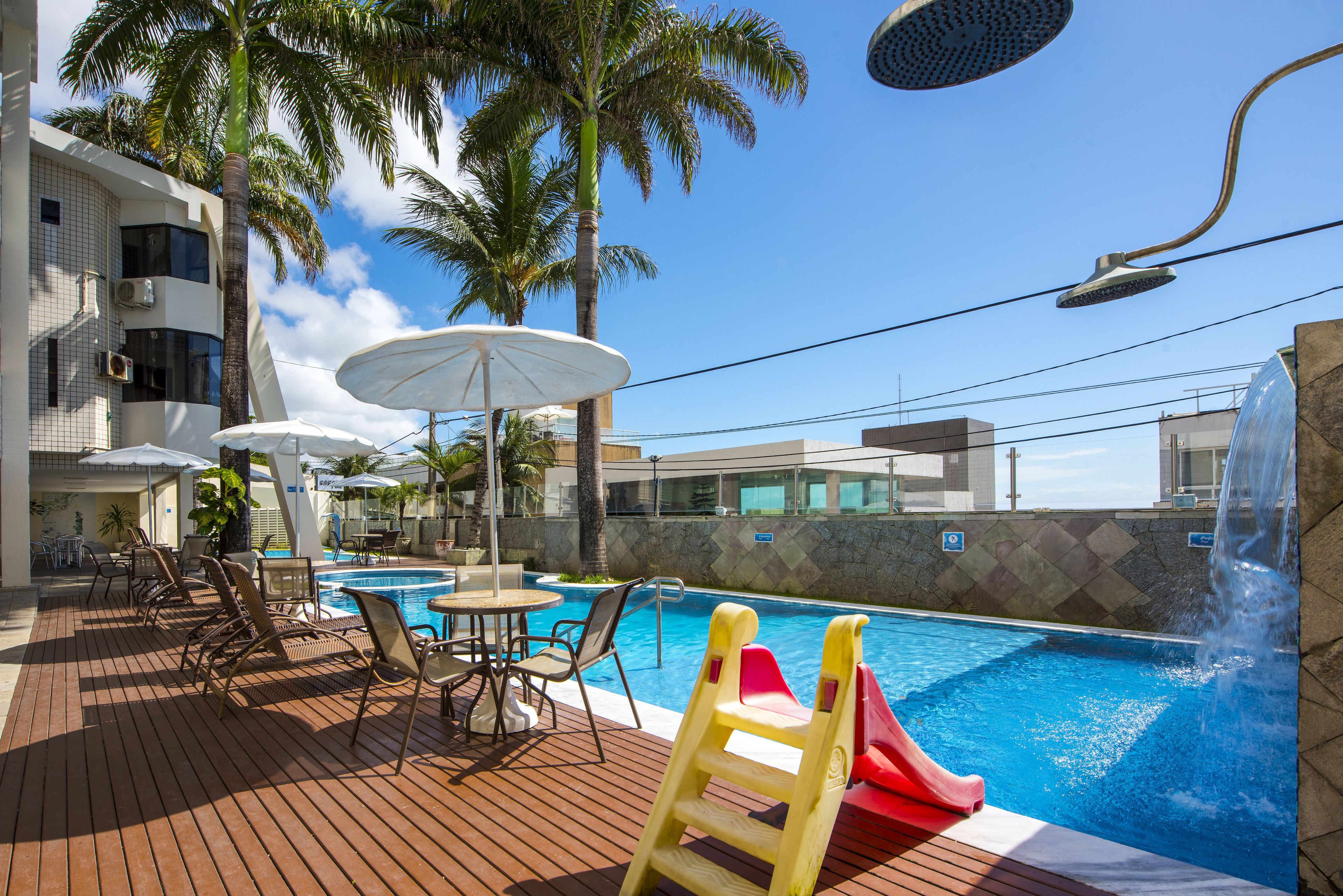 A pool area with lounge chairs, umbrellas, and a slide.