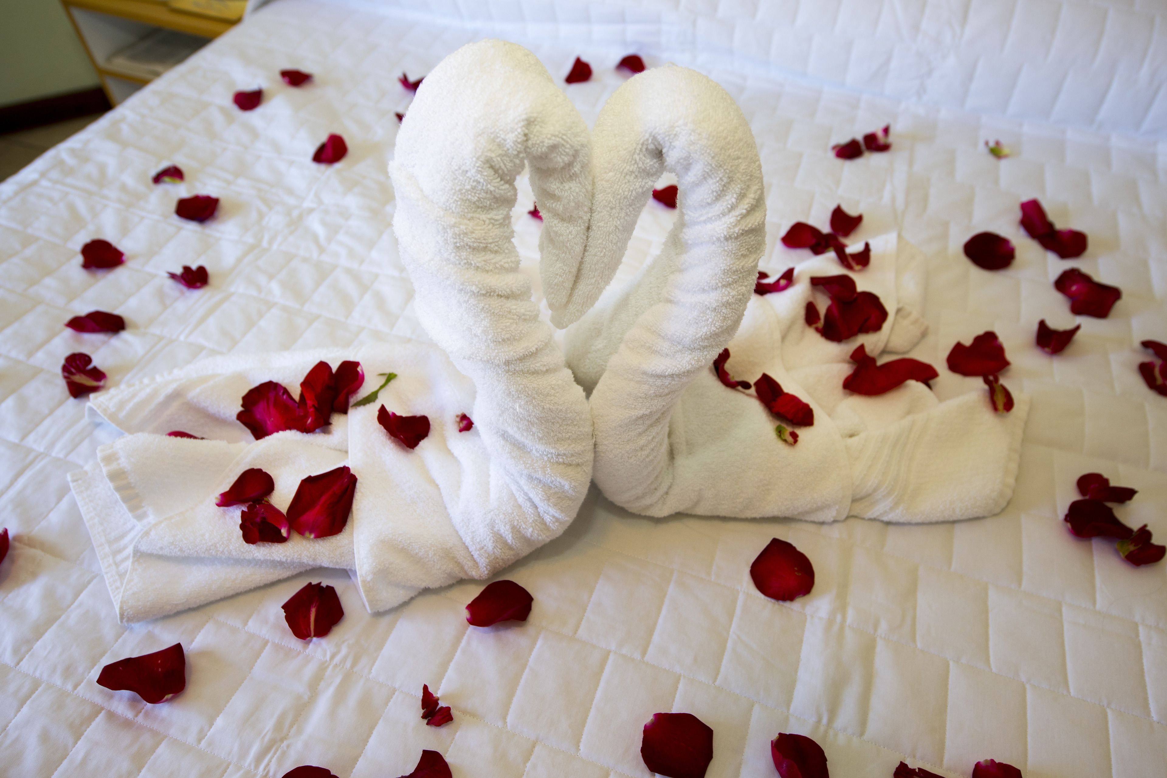 A bed with a white quilted bedspread and a towel arranged in a heart shape.