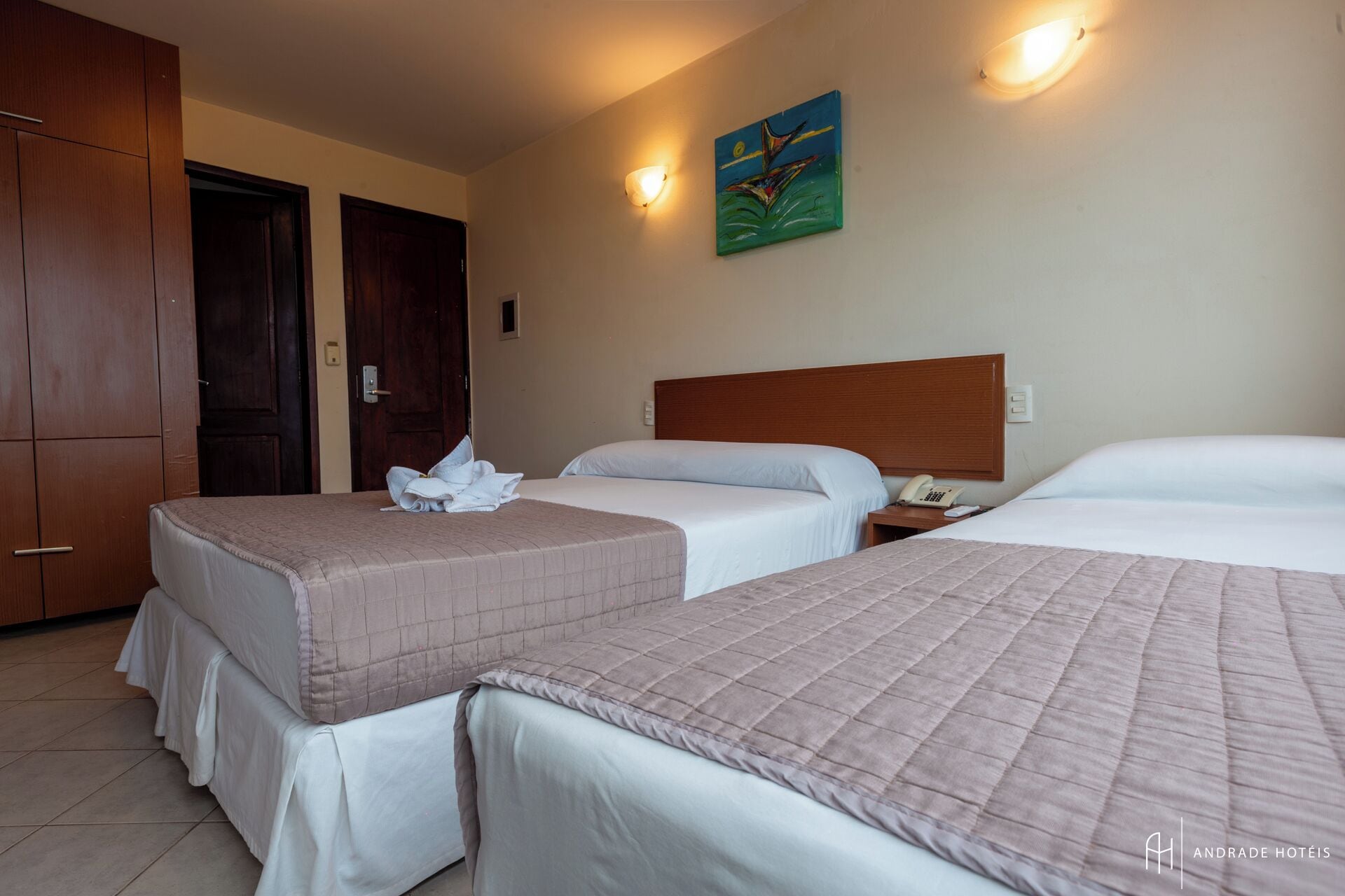 A hotel room with two beds, a wooden wardrobe, a painting on the wall, and a telephone on the nightstand.