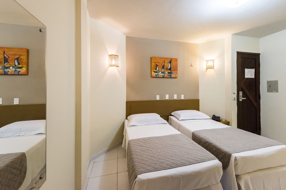 Quarto de hotel com duas camas de solteiro, cabeceira, quadro pendurado na parede e porta com placa.