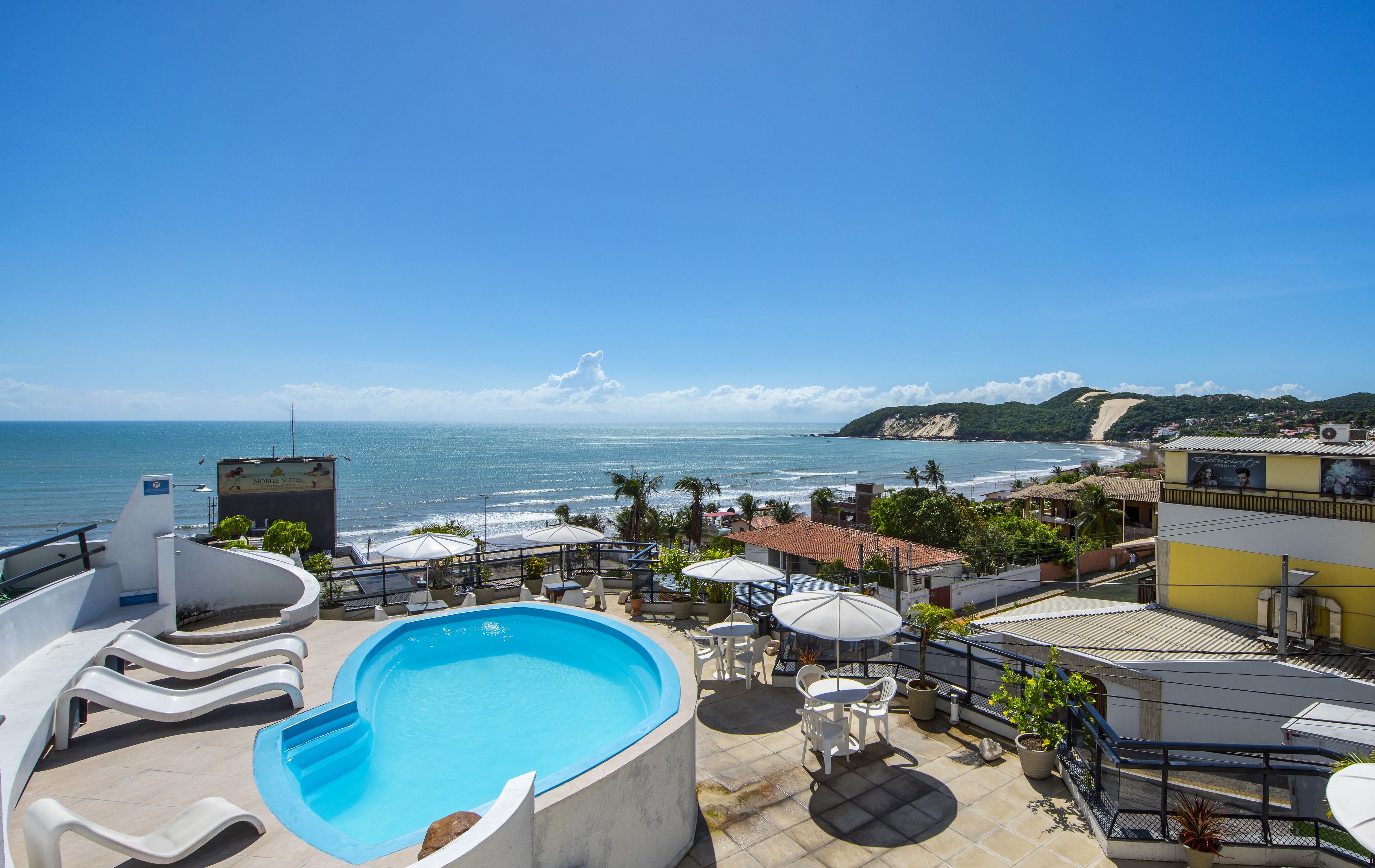 A rooftop pool area with a view of the ocean and a beach.
