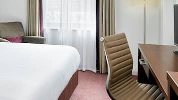 A hotel room with a bed, a desk with a television, a chair, and a window with curtains.
