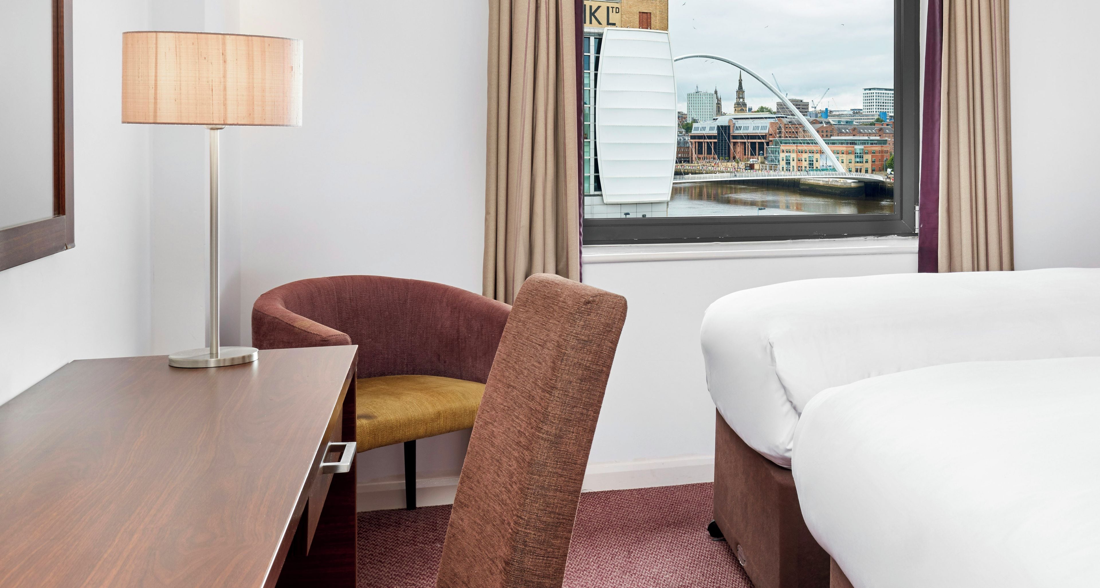 Una habitación de hotel con escritorio, silla, cama y ventana con vista a la ciudad.