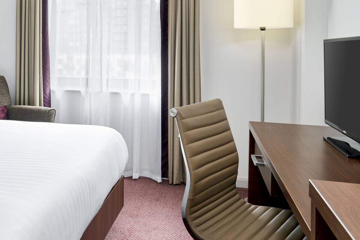 Una habitación de hotel con cama, escritorio con televisor, una silla y lámpara.