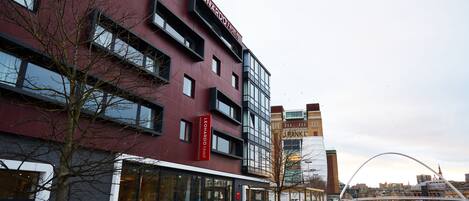 A modern hotel with a prominent red facade, large windows, and a visible name sign.