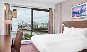 A hotel room with a large bed, a desk, a chair, and a view of a cityscape through a large window. - Leonardo Hotel Newcastle Quayside (Gateshead)