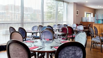 A restaurant with multiple tables and chairs, large windows, and a view of buildings outside.