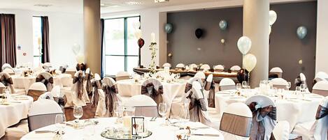Un salón de banquetes con mesas redondas dispuestas para un evento formal, con manteles blancos, cubertería y cristalería.