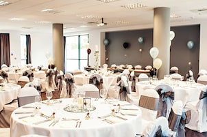 A banquet hall with round tables set for a formal event, featuring white tablecloths, silverware, and glassware.