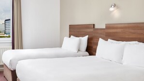 A hotel room with two beds, a wooden headboard, white bedding, a window with curtains, and a city view. - Leonardo Hotel Newcastle Quayside (Gateshead)