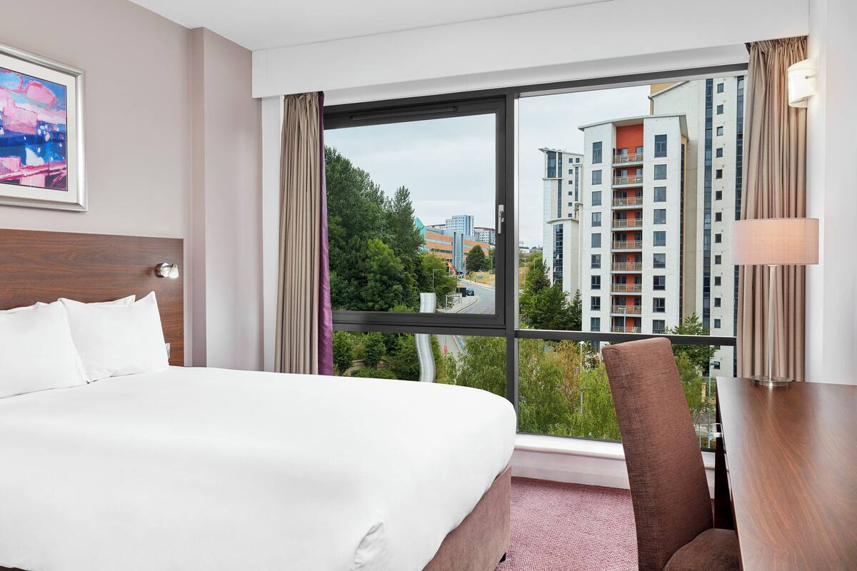 Una habitación de hotel con una cama grande, un escritorio y vistas de edificios altos.