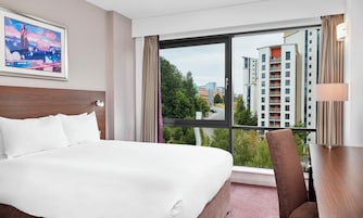 Una habitación de hotel con una cama grande, un escritorio y vistas de edificios altos.