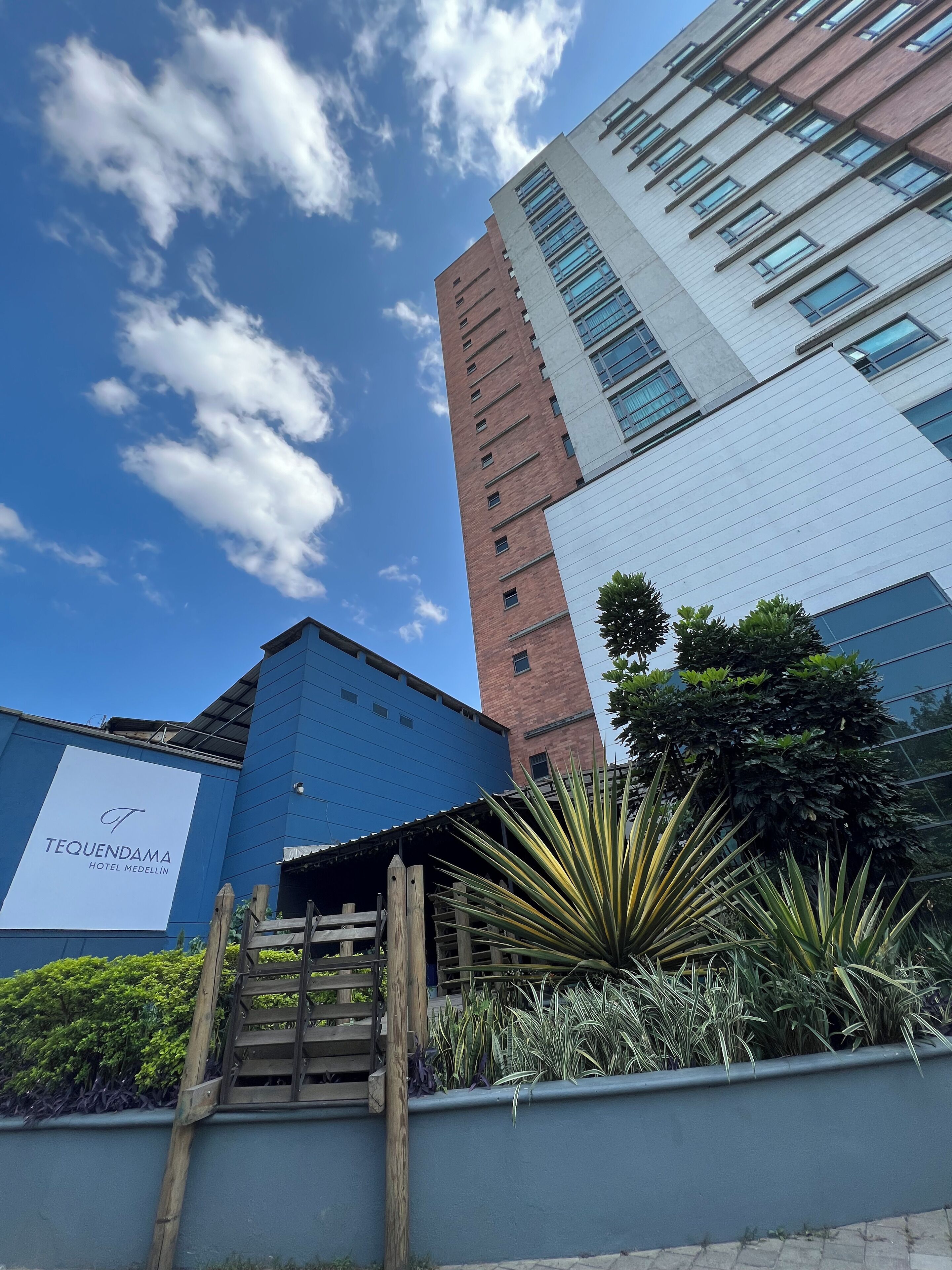 A modern hotel with a prominent sign for "Tequendama Hotel Medellín" and a view of the sky and clouds.