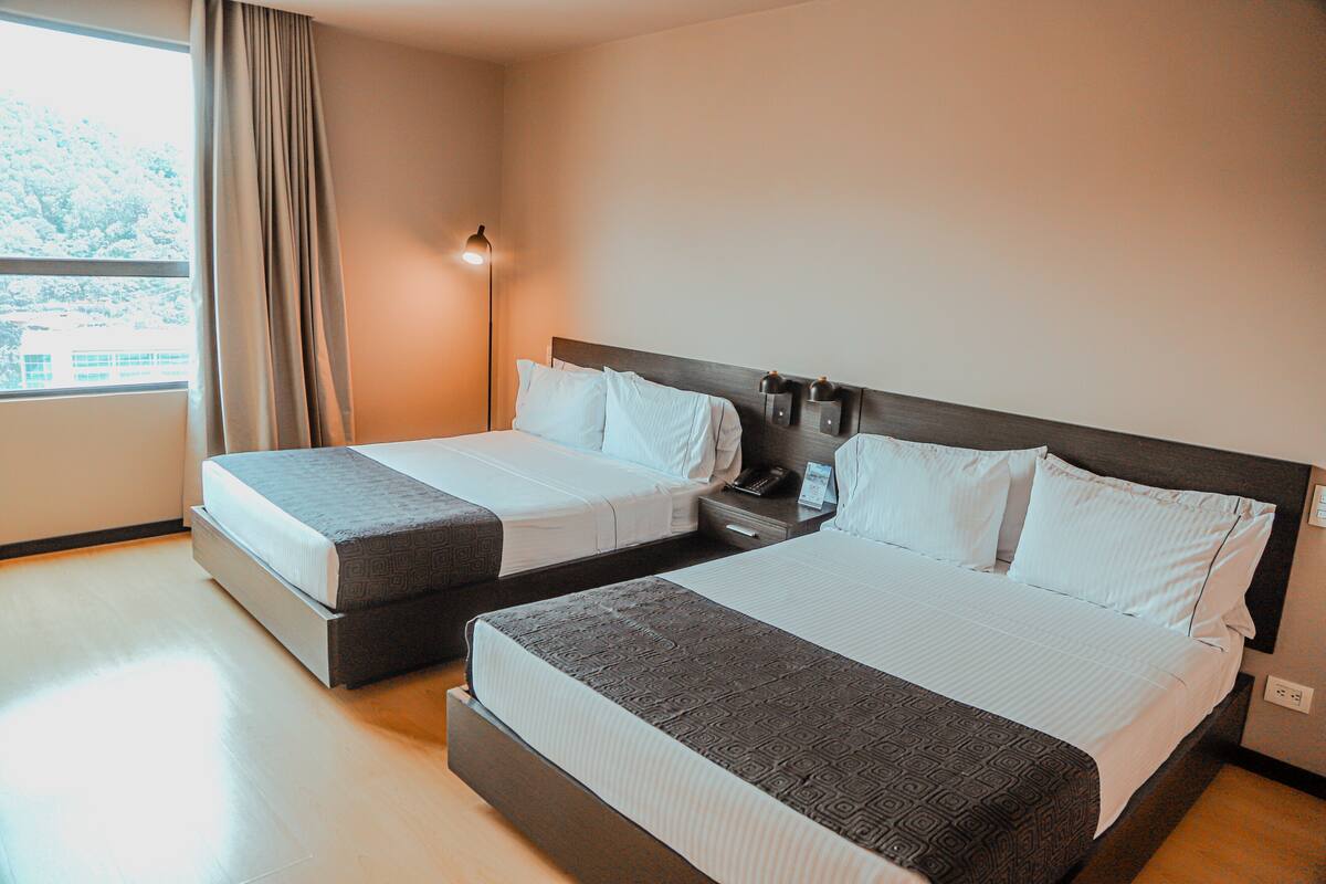 Een hotelkamer met twee bedden, een nachtkastje, een lamp en een raam met gordijnen.