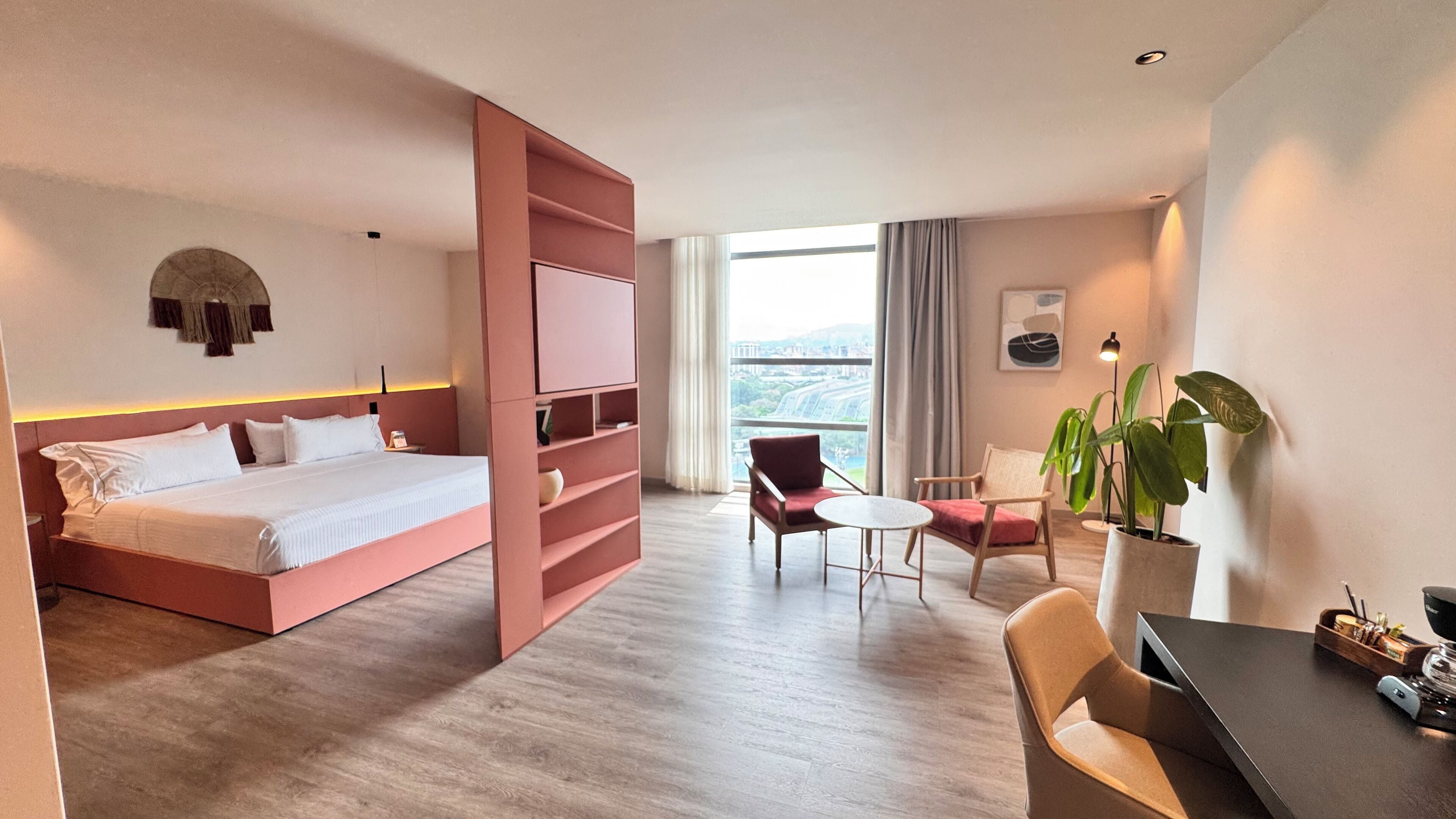 Habitación de hotel con cama, escritorio, silla, planta en maceta y vista de la ciudad.