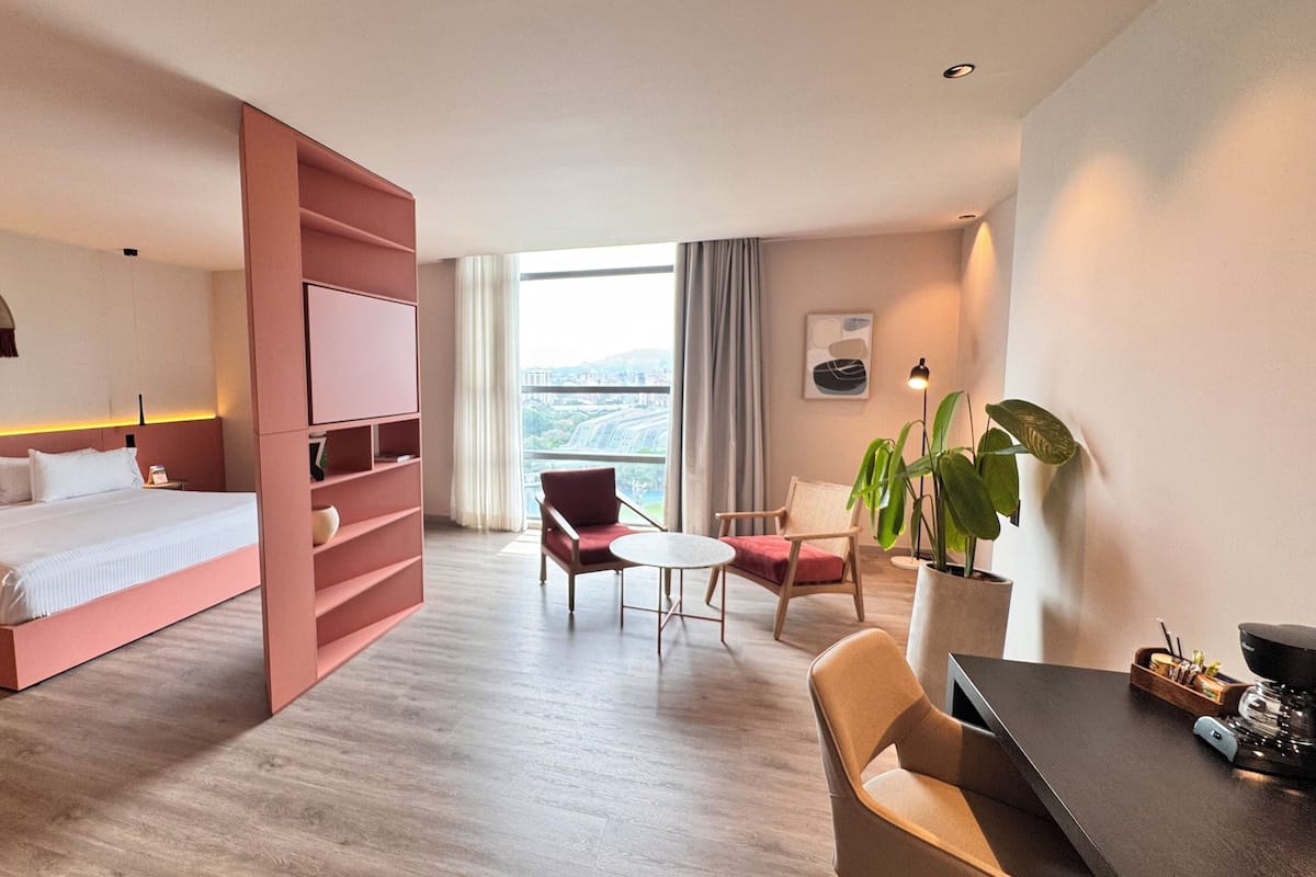 Een moderne hotelkamer met een groot bed, een bureau met stoel, een kleine tafel en een potplant.