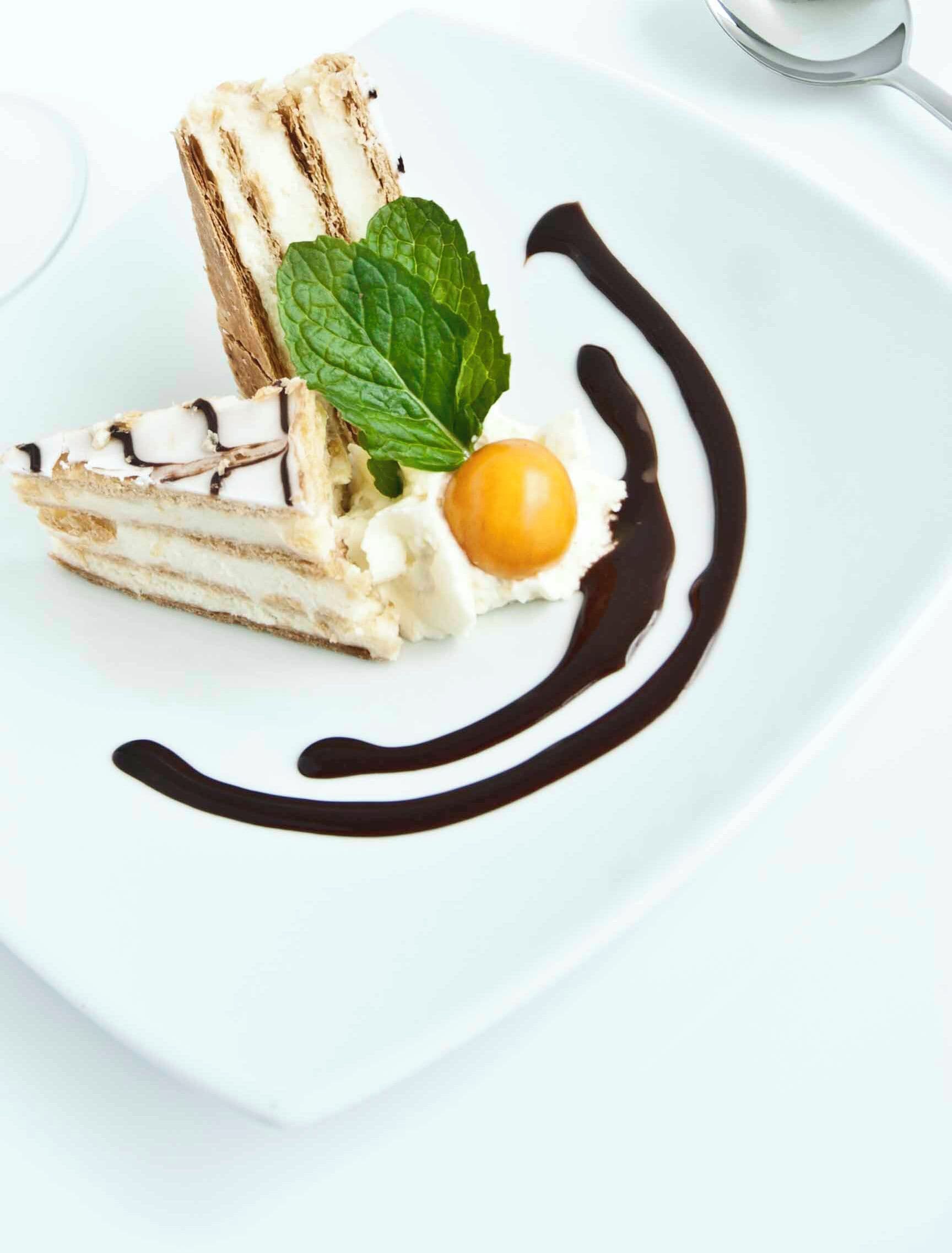 A dessert on a white plate with chocolate drizzle and a mint leaf.