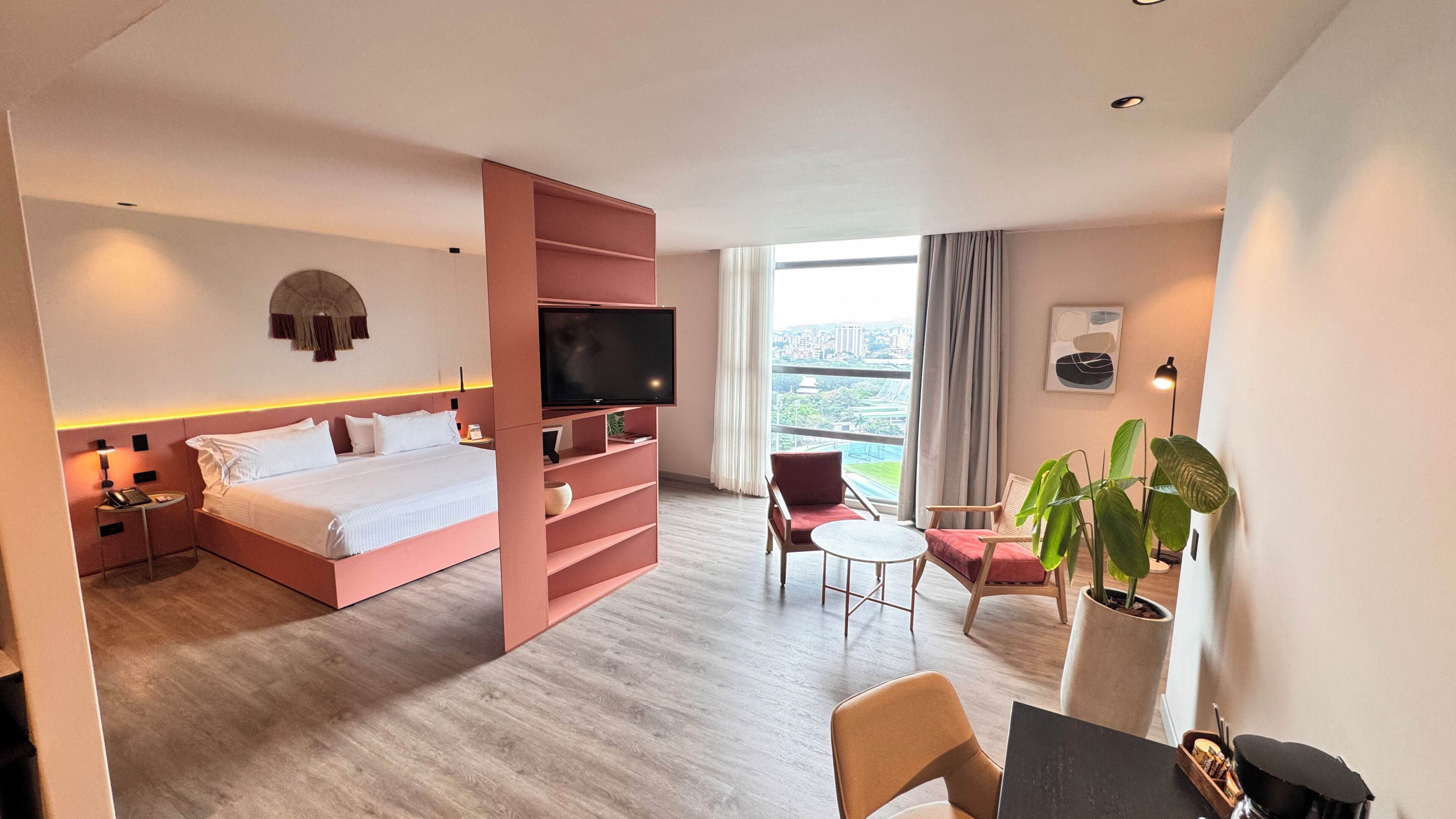 Habitación de hotel con cama, televisión, escritorio, silla y ventana grande con vista a la ciudad.