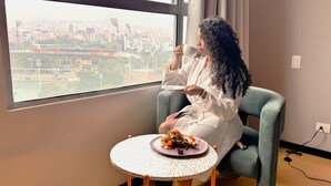 Une personne assise près d’une fenêtre, avec vue sur la ville, tenant une assiette.