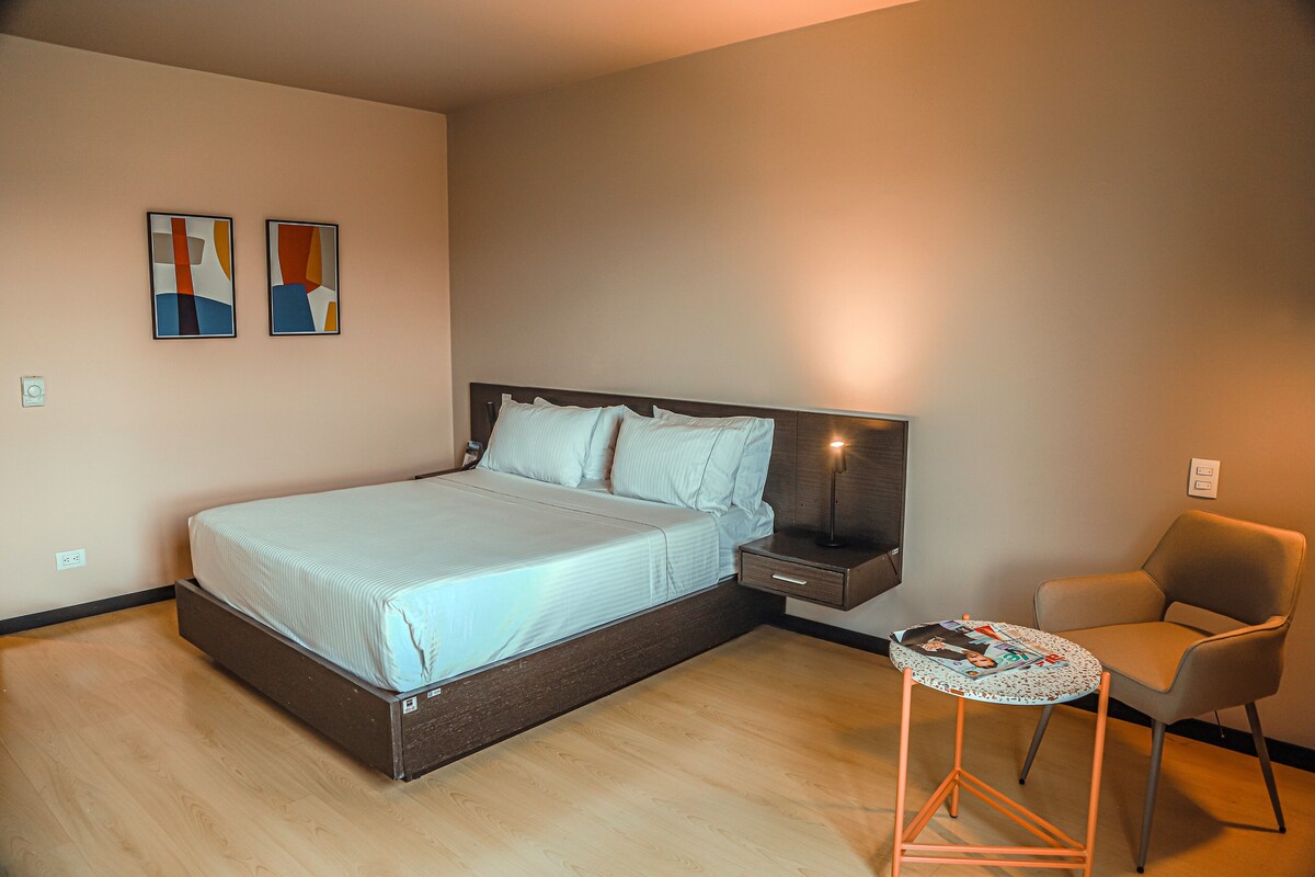 A bedroom with a bed, bedside table, chair, and two abstract paintings on the wall.