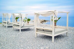 Een strand met vier witte, hemelbedden met draperende stof, geplaatst op een kiezelstrand.
