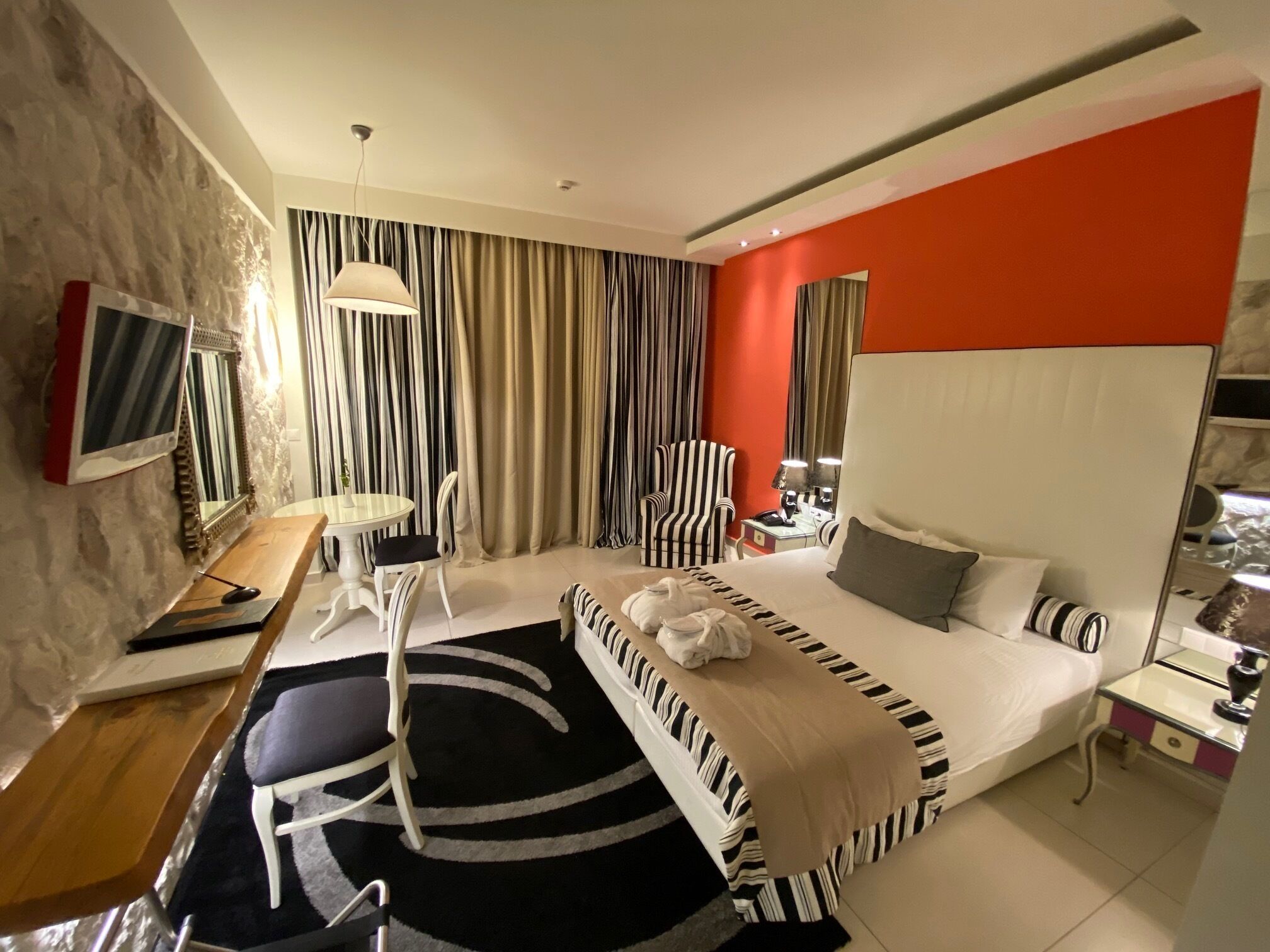 A modern hotel room with a large bed, a desk with a computer, a chair, a TV, and a window with curtains.