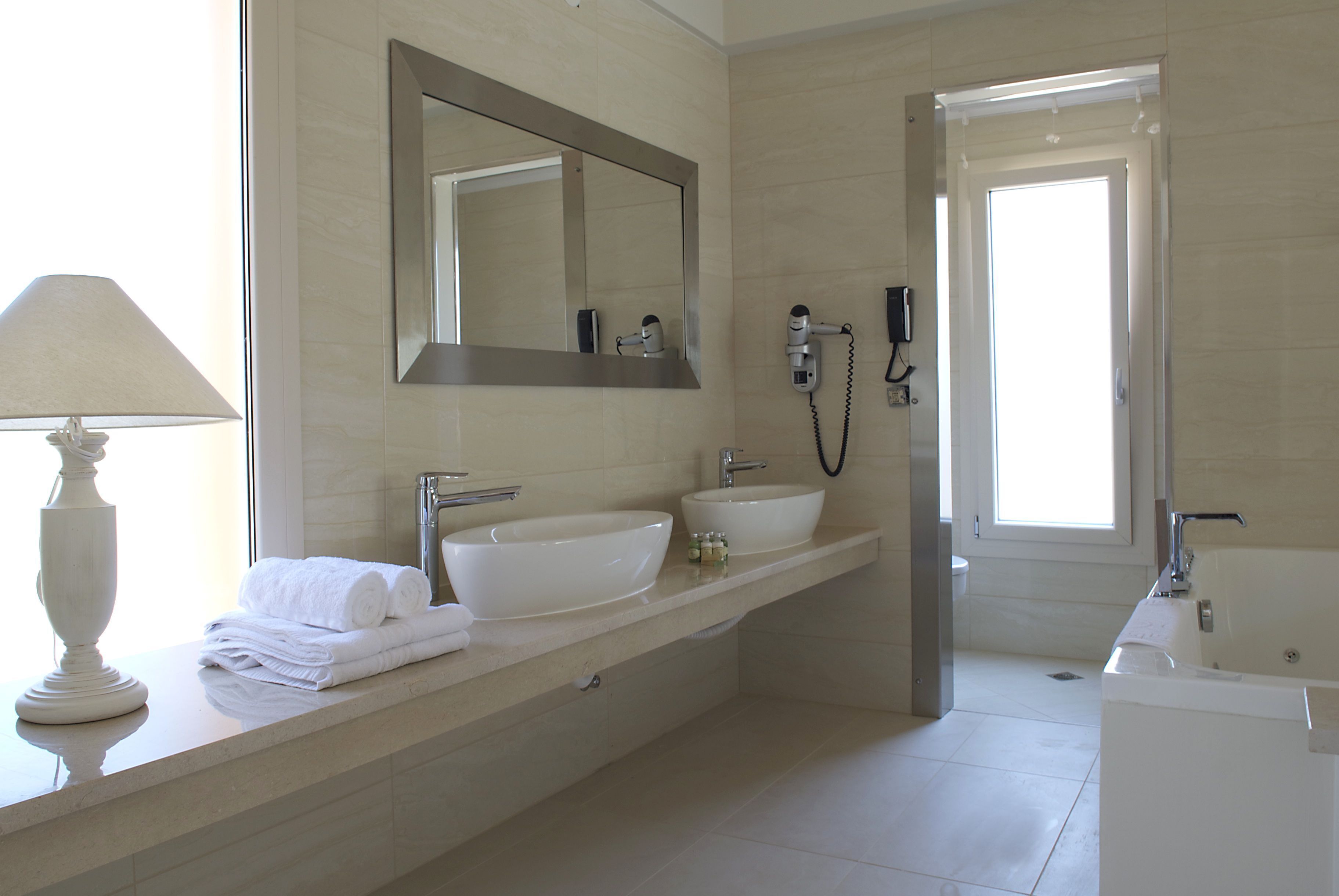 A modern bathroom with a large mirror, two sinks, a hairdryer, and a bathtub.