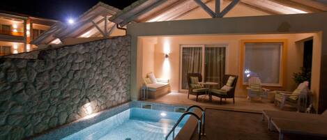 Una piscina con muro de piedra, sillas de descanso y una zona de estar con mesa y sillas.