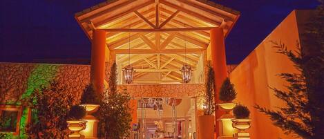 Fachada de hotel de piedra, estructura de techo de madera y dos grandes macetas con plantas.