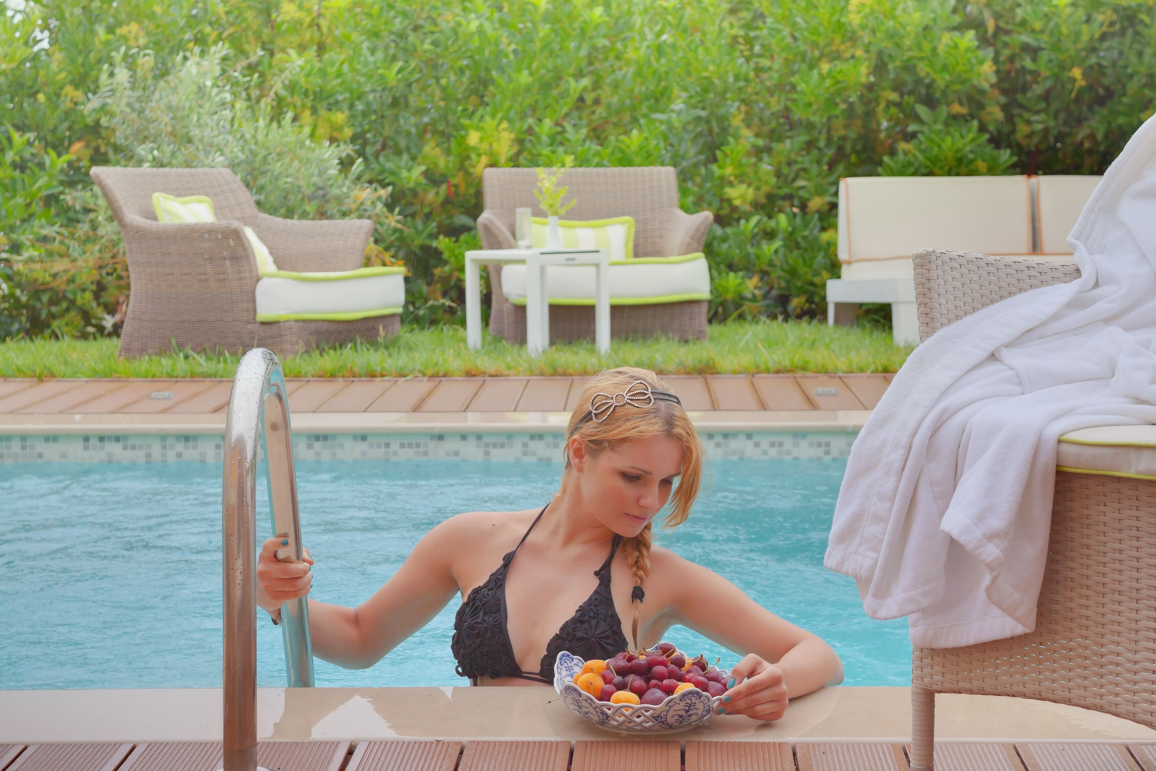 Zona de piscina con sillones de mimbre, una piscina y una mesa con un bol de fruta.