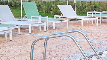 A pool area with lounge chairs and a striped umbrella, a clear view of the sea, and a tiled pool edge.
