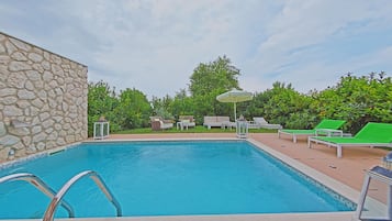 Una piscina con sillas de descanso y un muro de piedra.