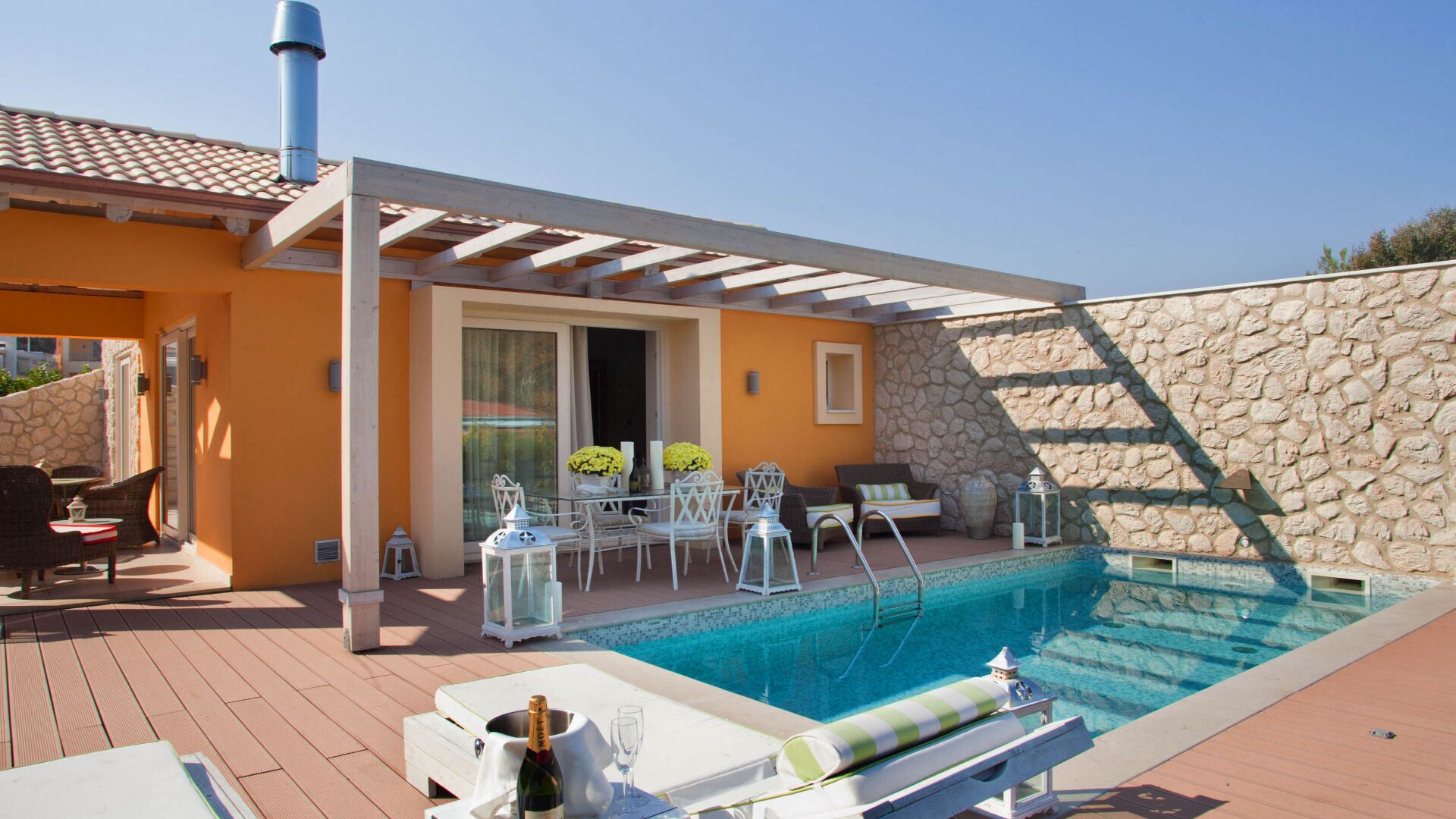 Un espace aménagé au bord de la piscine, avec un mur en pierre, des sièges d’extérieur et une pergola.
