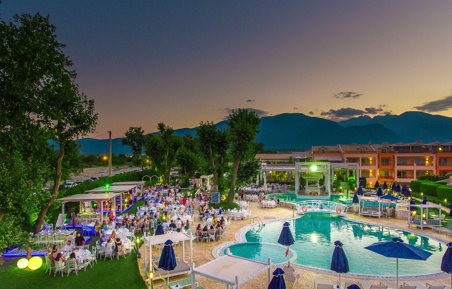 Un resort con comedor al aire libre y piscina central rodeada de sillas de descanso y sombrillas.