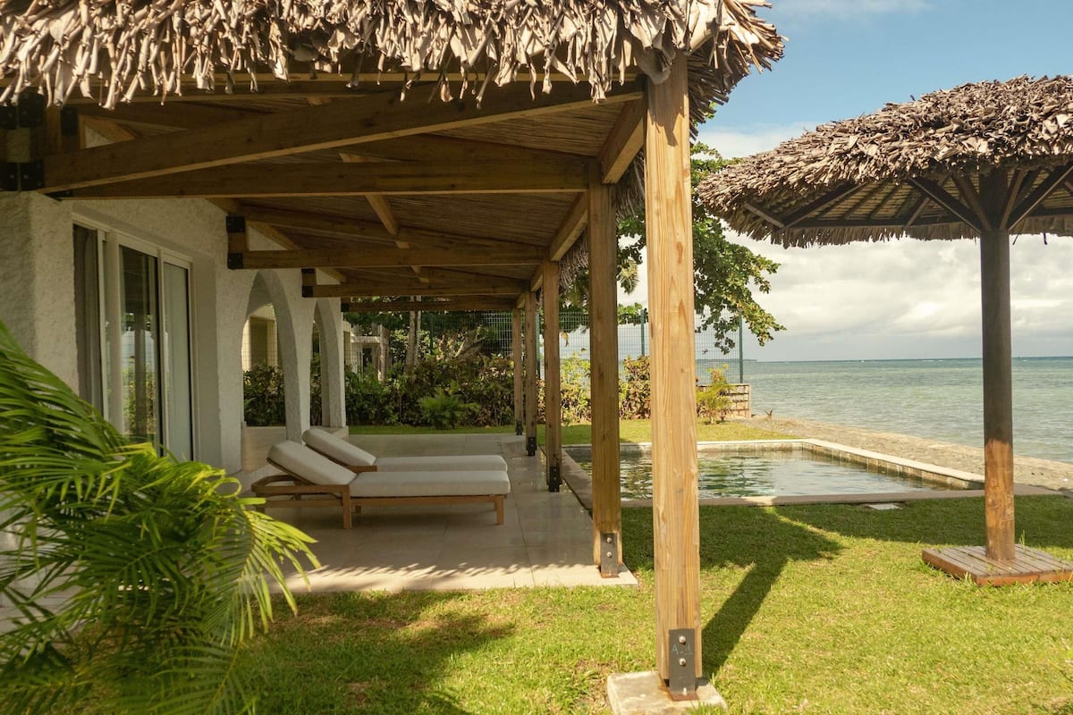 A covered outdoor area with lounge chairs, a pool, and a view of the sea.