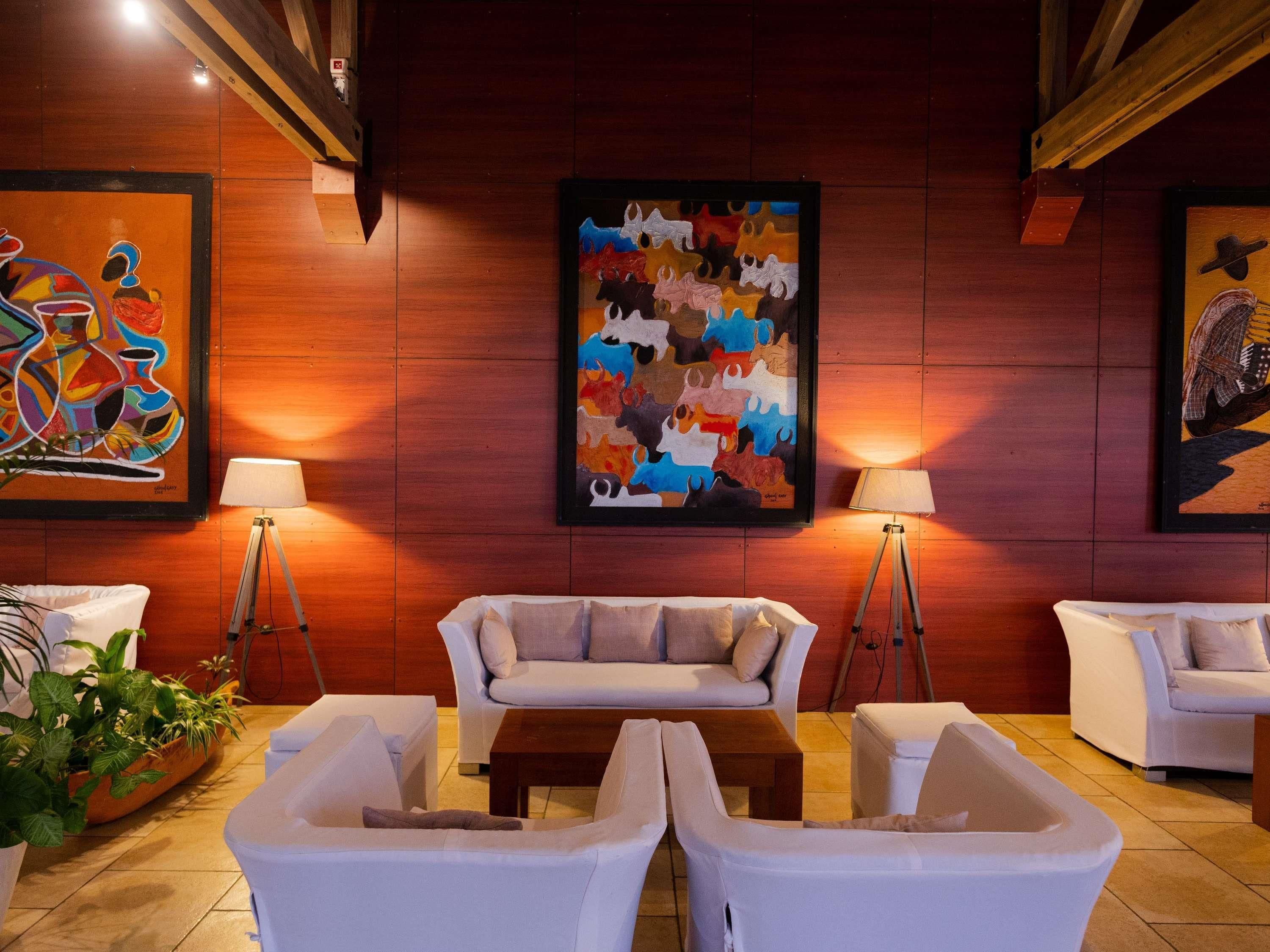 A modern living room with white furniture, a coffee table, and two floor lamps. There are three paintings on the wall.