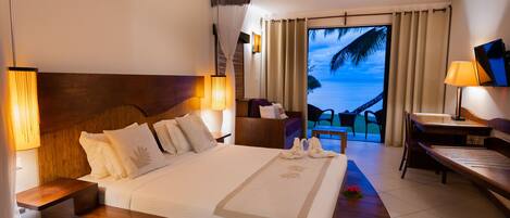 Una habitación de hotel con cama, mesitas de noche, escritorio, silla y vista al océano por la ventana.